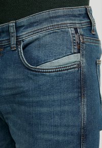 Jeans aus Denim mit einem hellblauen Waschung, orangefarbenen Nähten, einer Fronttasche mit einem dezent kontrastierenden Besatz und traditionellem Fünf-Taschen-Design.