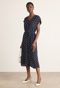 Navy polka dot midi dress with a v-neck, short sleeves, and a tied waist. Made from lightweight fabric with a soft texture.