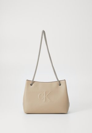 Borsa in finta pelle beige con tracolla in catena argentata, caratterizzata da un logo "cK" impresso e una forma strutturata. Design semplice e moderno.
