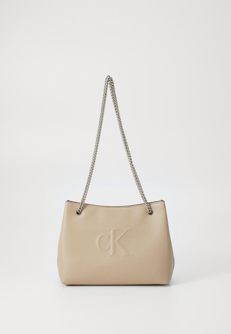 Borsa in finta pelle beige con tracolla in catena argentata, caratterizzata da un logo "cK" impresso e una forma strutturata. Design semplice e moderno.
