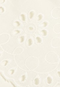 Tejido blanco con intrincados bordados que presentan recortes circulares y patrones ondulados, creando una apariencia texturada, similar a encaje.