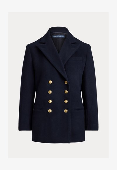 Divkrūšu zila žakete no vilnas ar lieliem zelta pogām, ar izteiktiem atlokiem un sānu kabatām. Rādot krūšu kabatu un pielāgotu piegriezumu.