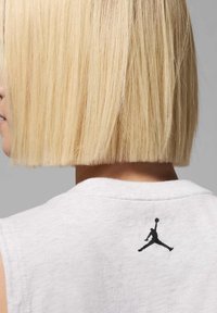 Camisa sin mangas blanca con un logotipo de Jumpman negro en la parte posterior. El material parece suave con una textura lisa; sin patrones visibles.