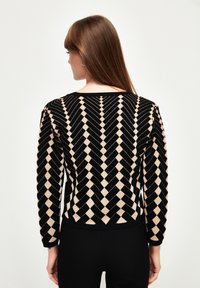 Pull noir et beige à motifs avec un design géométrique en losanges, doté de manches longues et d'un col rond, fabriqué à partir d'un doux matériau en tricot.