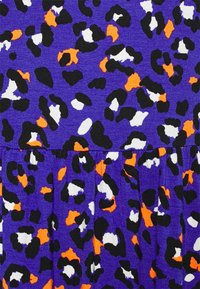 Lila tyg med ett mönster i leopardtryck. Accenter i svart, vitt och orange med en texturerad yta och samlade veckdetaljer.