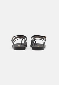 Black flat sandals featuring a smooth surface, slender straps, and a gold-tone buckle accent. Design emphasizes minimalism and comfort.