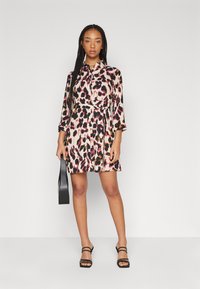 Klänning med leopardmönster i mjukt tyg med långa ärmar och skjortkrage. Har en midja som är åtdragen och en svajande kjol. Svarta sandaler med remmar.