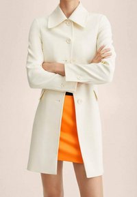 Witte, knielange jas met een grote kraag, knopen aan de voorkant en zijzakken, gecombineerd met een oranje minirok. Gladde textuur.