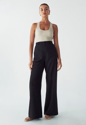 Ribbed light beige tank top and high-waisted black wide-leg trousers. The fabric appears smooth with a clean, tailored fit and minimal detailing.