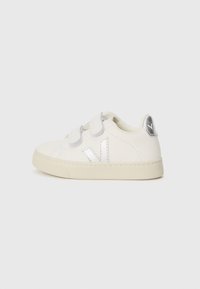 Hvite sneakers med sølvfarget detaljer, borrelåsreimer, strukturert gummisåle, rund tå og en fremtredende V-logo på siden.