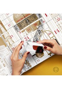 Calendrier de l'avent au design or et blanc, avec une porte ouverte révélant un flacon de vernis à ongles à bouchon rouge et une teinte de vernis rouge.