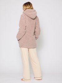 Miękki, pluszowy, beżowy hoodie z dużym kapturem i kieszeniami po bokach, w połączeniu z luźnymi, kremowymi spodniami z czarnym wykończeniem na dole.