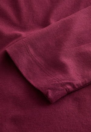 Artimuose maroon audinio raukšlėse matomos siūlės palei apdailos kraštą.