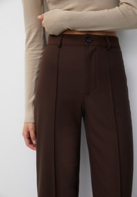 Bruine op maat gemaakte broeken met een gladde textuur, voorzien van een knoopsluiting en zijnaden, getoond met een beige langemouwen top.