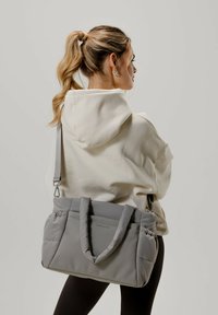 Borsa a tote grigia imbottita con doppie maniglie e tracolla rimovibile. Texture liscia, forma rettangolare, con branding sottile e tasche laterali.