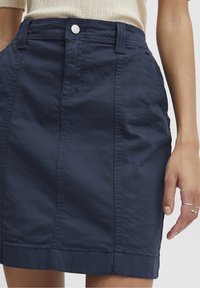 Jupe en coton bleu marine à taille haute, avec des boutons à l'avant et des poches latérales. Présente des coutures visibles et une silhouette droite et ajustée.