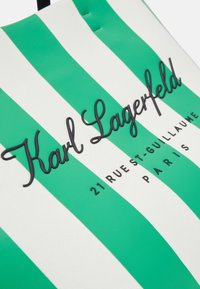 Sac rayé vert et blanc avec logo cursif noir "Karl Lagerfeld" et texte "21 Rue St-Guillaume Paris" en dessous.