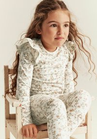 Puuvillaiset pyjamat, joissa on kukkakuosiset kankaat, röyhelöhihat ja pehmeät pastellivärit. Kankaassa on pieniä eläinkuvastoja kukkien keskellä.