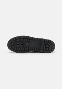 Suela de zapato de goma negra con profundos patrones de perfil y logotipo de marca en relieve para mejorar el agarre y la tracción. Textura suave, material duradero.