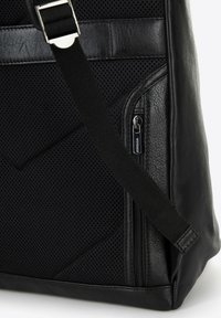 Borsa in pelle nera con una parte anteriore testurizzata e perforata, una tasca laterale con zip e una tracolla regolabile. Include dettagli decorativi di design geometrico.