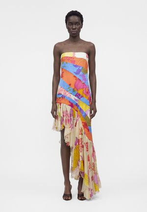 Kvinde iført en stropløs, asymmetrisk kjole med farverige blomster- og abstrakte mønstre, kombineret med sorte åbne hæle.