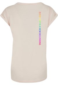 Helles rosa T-Shirt mit aufgerollten Ärmeln und geradem Saum. Auf der Rückseite befindet sich der regenbogenfarbene Text: "JEDER TAG IST EIN NEUER BEGINN."