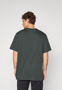 Mørkegrøn, kortærmet t-shirt, lavet af bomuldsstof, afslappet pasform, rund halsudskæring, synlige sømdetaljer på kanten og ærmerne.