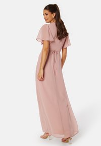 Robe maxi en rose pâle, fabriquée dans un tissu léger. Dotée de manches flottantes, d'une taille cintrée avec un lien et d'une jupe fluide.