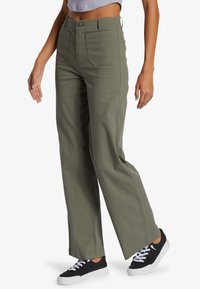 Groene wijde broek van een katoenmix, met een knoopsluiting, voor- en achterzakken, en een rechte zoom. Gekoeld met zwarte sneakers.