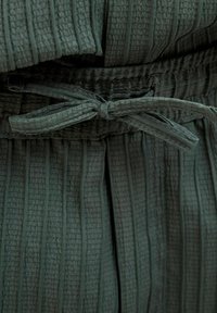Tissu texturé vert foncé avec des rayures verticales, mettant en valeur une ceinture nouée. Le design présente une apparence douce et superposée.