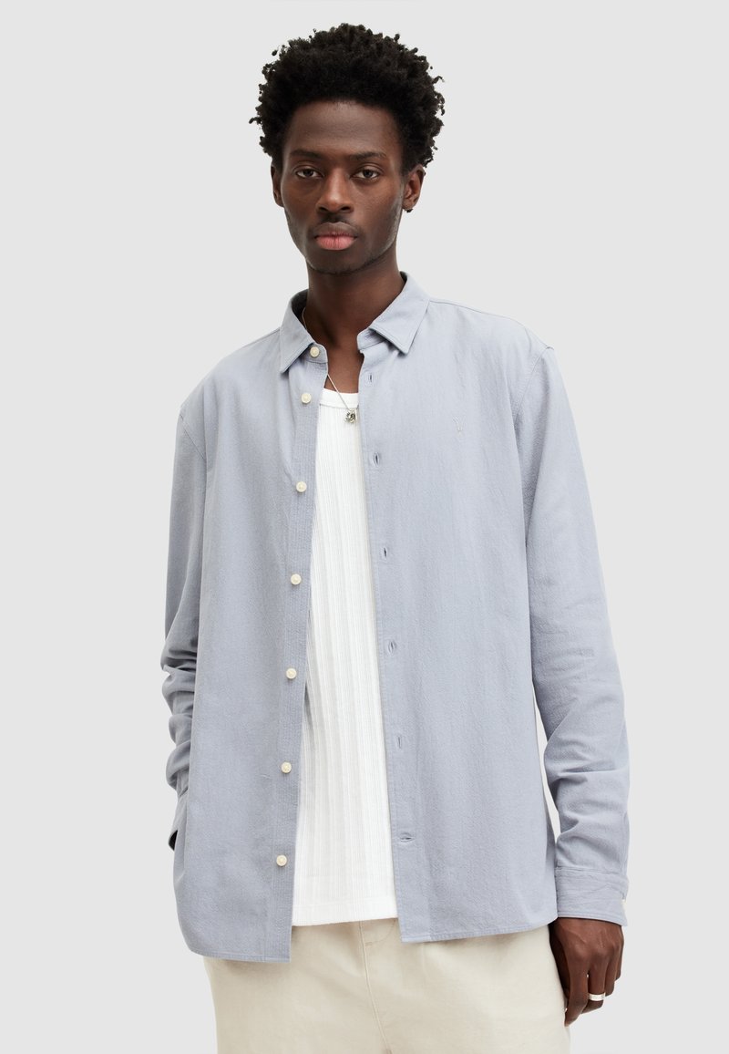 Lichtblauw button-up shirt van zachte stof, met een klassieke kraag, lange mouwen en witte knopen. Draagt over een gestructureerd wit T-shirt.