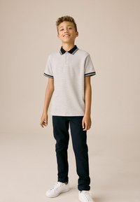 Kortærmet polo-shirt i lysegrå med et struktureret mønster, sort krave og stribede ærmer; parret med mørke bukser og hvide sneakers.