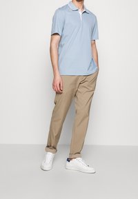 Polo de color azul claro con cuello blanco, combinado con pantalones beige y zapatillas blancas. El conjunto presenta un ajuste relajado y mangas cortas.