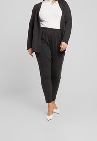 Ciemnoszary, dwuczęściowy strój składający się z kardiganu z długim rękawem i dopasowanych spodni, zestawiony z białymi, szpiczastymi szpilkami, na neutralnym tle.