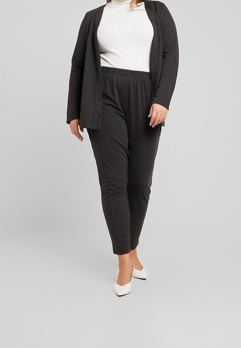 Ciemnoszary, dwuczęściowy strój składający się z kardiganu z długim rękawem i dopasowanych spodni, zestawiony z białymi, szpiczastymi szpilkami, na neutralnym tle.