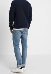 Felpa girocollo blu marina con polsini a coste, abbinata a jeans azzurri con orli arrotolati e sneakers bianche con dettagli neri.