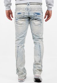 Jeans in denim azzurro chiaro con lavaggio sbiadito, progettati con tasche posteriori e logo "CIPO & BAXX" sulla vita. Accentuati da cuciture a contrasto.
