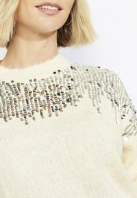 Kreemjas kootud kampsun, millel on litritega kaunistatud kaelus erinevates värvides. Pehme tekstuur, lõdva istuvusega ja soonikkoes varrukasuu.