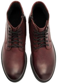 Brązowe skórzane botki o gładkim wykończeniu, czarne sznurowadła i zamki błyskawiczne po bokach. Okrągły czubek i teksturowana wewnętrzna podszewka.