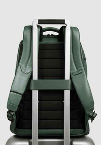 Zaino in pelle verde con schienale imbottito in tessuto nero, spallacci regolabili e maniglia telescopica argentata per il fissaggio ai bagagli.