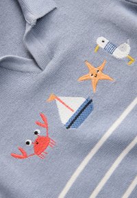 Lyseblåt strikket stof med broderede motiver: en rød krabbe, en gul søstjerne, en hvid sejlbåd med blå detaljer og en and.