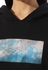 Haut à capuche noir présentant une zone rectangulaire avec un design abstrait bleu et rose, fabriqué en tissu doux avec une impression texturée.