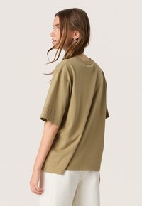 Tricou oversized de culoare verde măsliniu, din bumbac moale. Mâneci scurte cu detaliu brodat pe mâneca stângă. Decupaj rotund la gât.