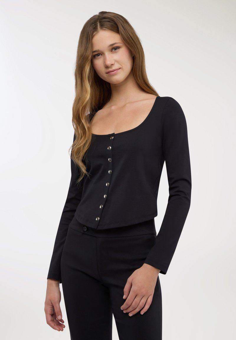 Top nero a maniche lunghe con scollo a barca e chiusura con bottoni sul davanti. Il tessuto è liscio ed elastico, offrendo una silhouette aderente.