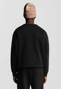 Felpa nera con una vestibilità rilassata, polsini a costine e scollatura a girocollo, abbinata a pantaloni coordinati. Un berretto in maglia beige completa il look.