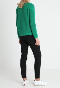 Groene gebreide trui met een textuurontwerp, gecombineerd met zwarte aansluitende broek en witte sneakers met kleurtinten op de hak.