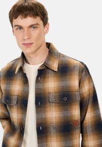 Brun og marineblå plaidskjorte lavet af flannel. Har to brystlommer og et mærketags. Knaplukning med krave.