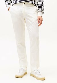 Pantaloni bianchi in cotone con una vestibilità rilassata, dotati di tasche laterali e vita con cordoncino. Abbinati a sneakers bianche e a un maglione a righe.