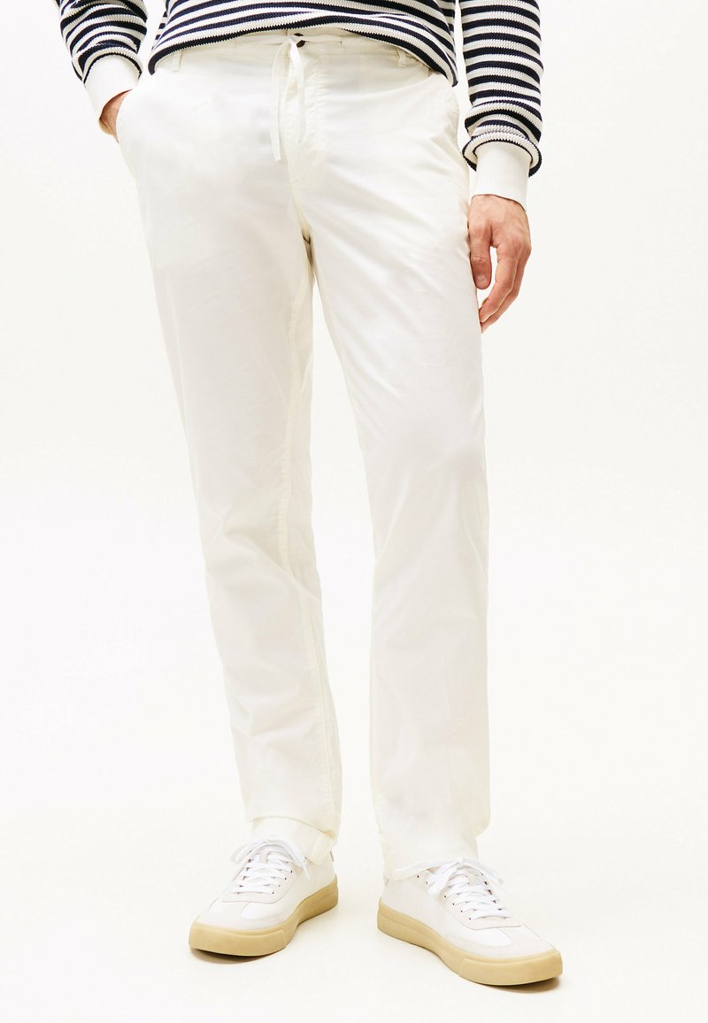 Pantaloni bianchi in cotone con una vestibilità rilassata, dotati di tasche laterali e vita con cordoncino. Abbinati a sneakers bianche e a un maglione a righe.