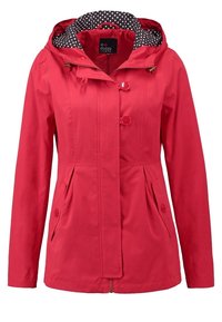 Veste rouge pour femme avec capuche, deux poches à rabat boutonnées à l'avant, fermeture par boutons et fermeture éclair, et doublure noire à pois à l'intérieur de la capuche.